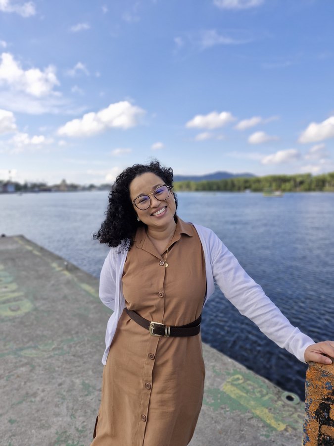 Letícia sorrindo em um píer ao mar